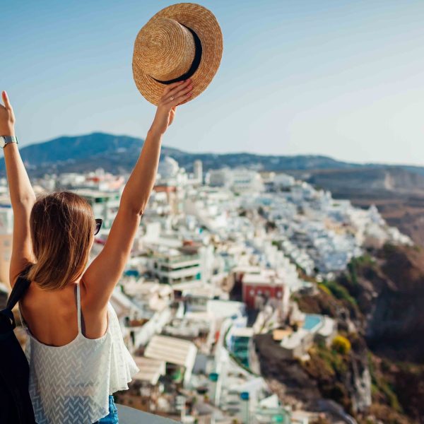 Woman tourist raised arms looking at Caldera sea landscape in Fira, Santorini island. Traveling during summer vacation